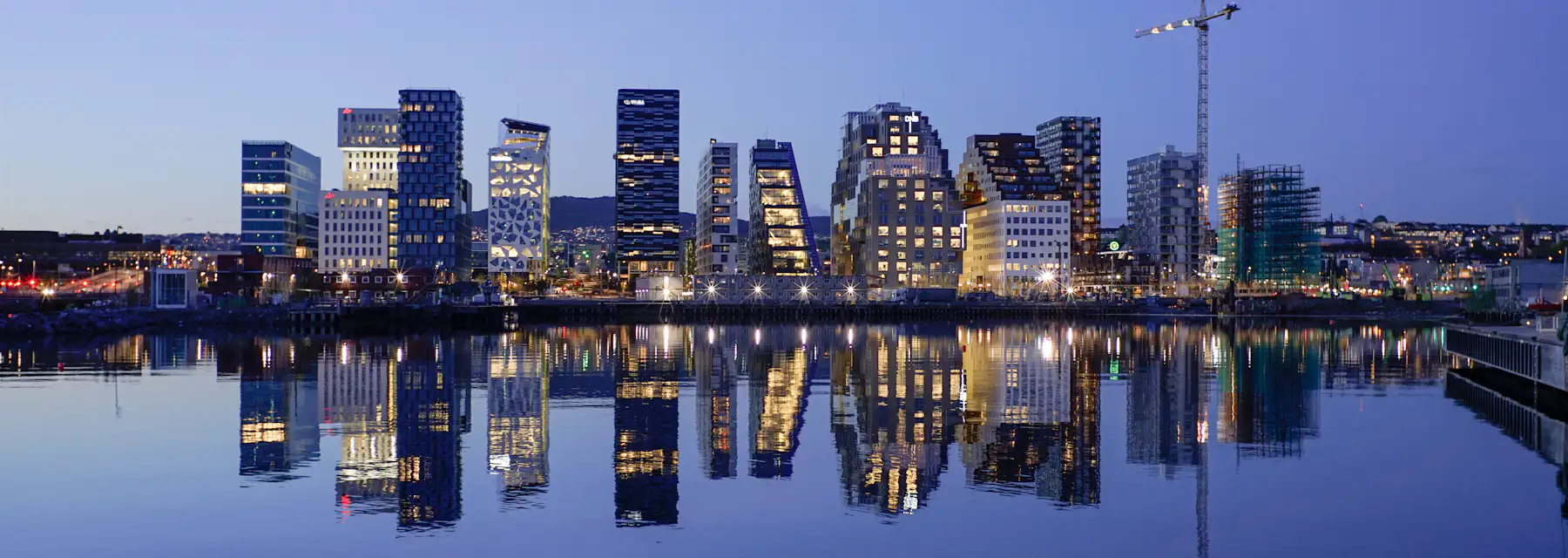 Oslo's waterfront skyline at dusk, modern glass high-rises reflected in the still fjord